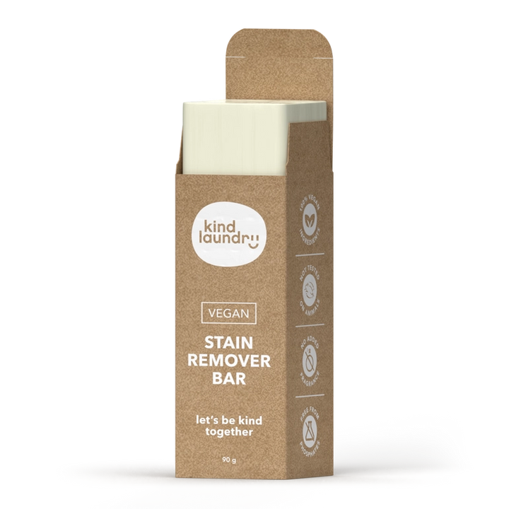 A brown cardboard box labeled Vegan Laundry Stain Remover Bar 90g by Kind Laundry stands upright, partially open to reveal the white bar inside. The packaging features symbols for eco-friendly, phosphate-free, and vegan attributes.