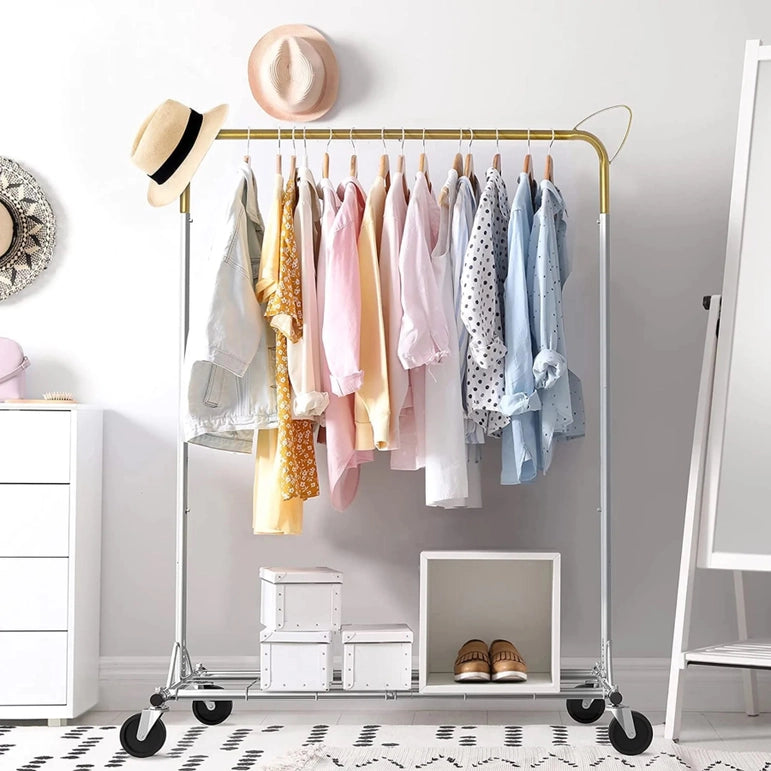 The Above Edge Hanging Garment Rack with Shelf displays pastel and patterned shirts, jackets, and a dangling hat. Below, white storage boxes accompany brown shoes. In the background, a decorative mirror complements the scene beside a dresser.