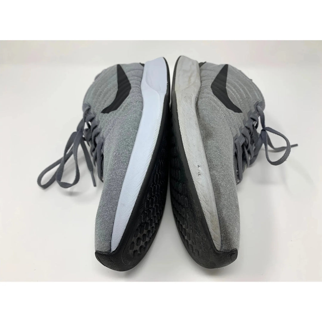 Gray athletic shoes are shown side by side on a white surface, highlighting the more worn sole of the right shoe. With laces and a black pattern on the bottom, they’re ideal for a quick touch-up using Shoe Eraser SOAK, Sneaker Detergent by SneakERASERS.