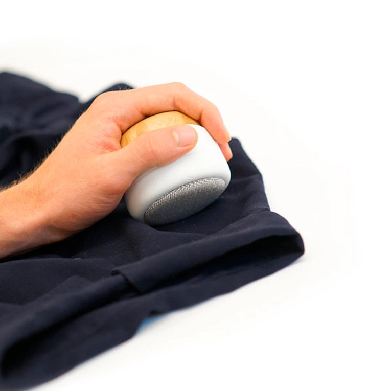 A person uses the Fuzz Off Reusable Lint Remover by Full Circle Home on a dark garment against a white background. The wooden-handled tools micro-bristle fabric removes lint, fuzz, and pet hair, providing an eco-friendly way to keep clothes pristine.