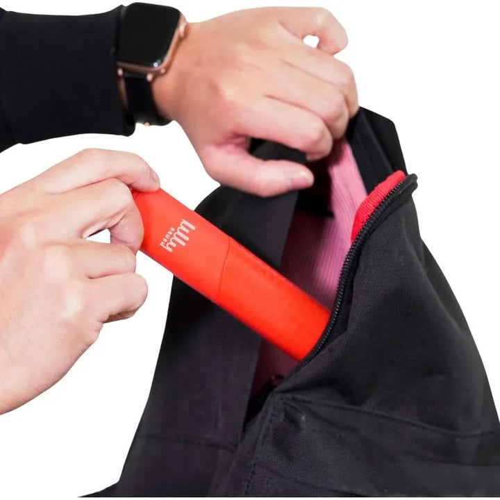 A person wearing a smartwatch places the Lilly Brush - Be Forever Furless Mini, known for being a lint magnet, into a black bag with a pink interior. The focus is on the item and hands.