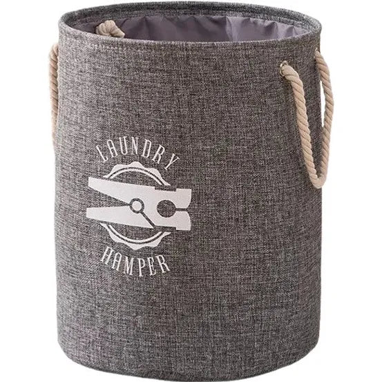 The All Things Laundry Cotton and Linen Collapsible Clothes Laundry Hamper is a gray cylindrical fabric basket with two rope handles, adorned with a clothespin graphic and the words Laundry Hamper in bold white letters, available in two colors.