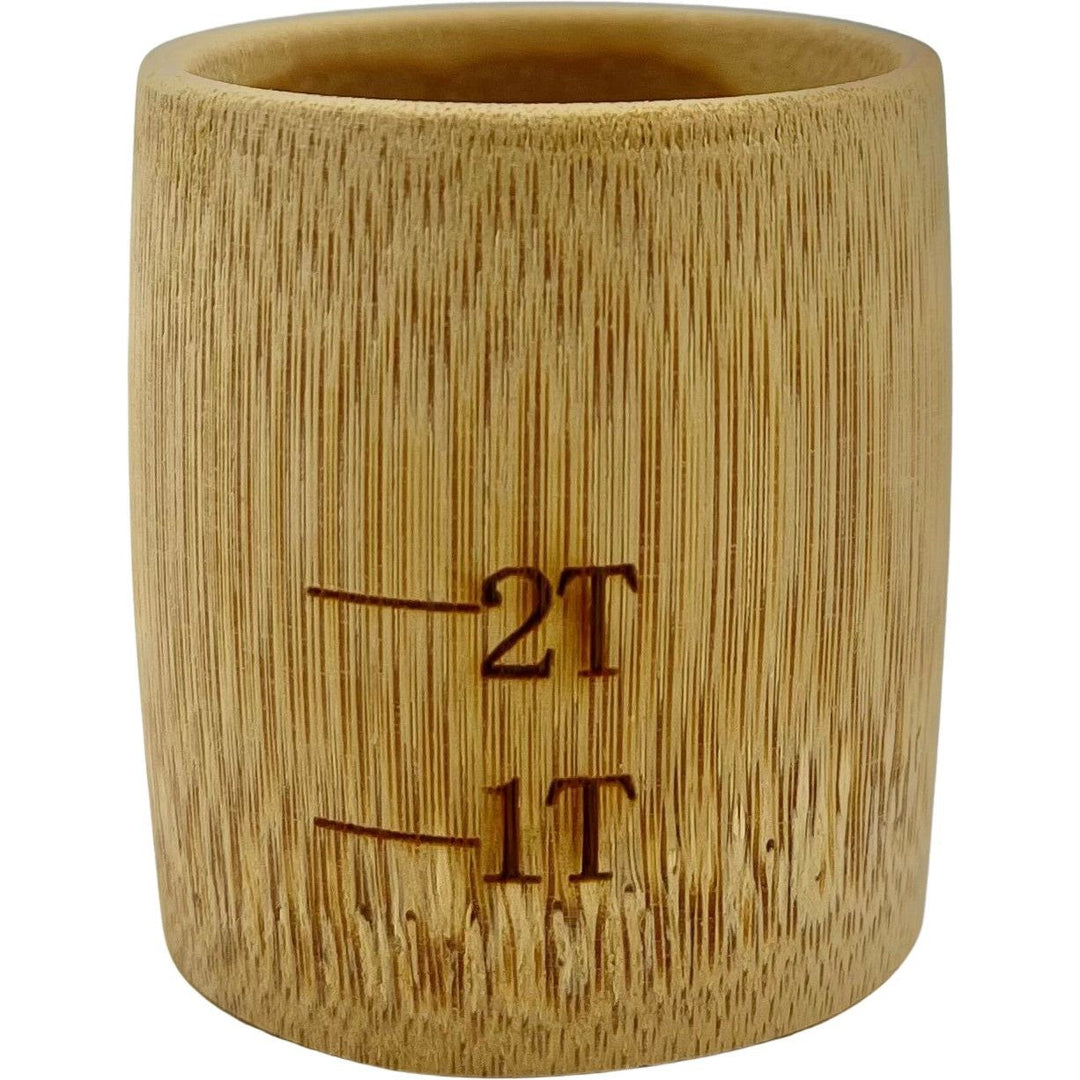 The BAMBOO Measuring Cup by Root and Splendor features a cylindrical design with 1 and 2 tablespoon engravings, providing a natural aesthetic with its sustainable wood grain.